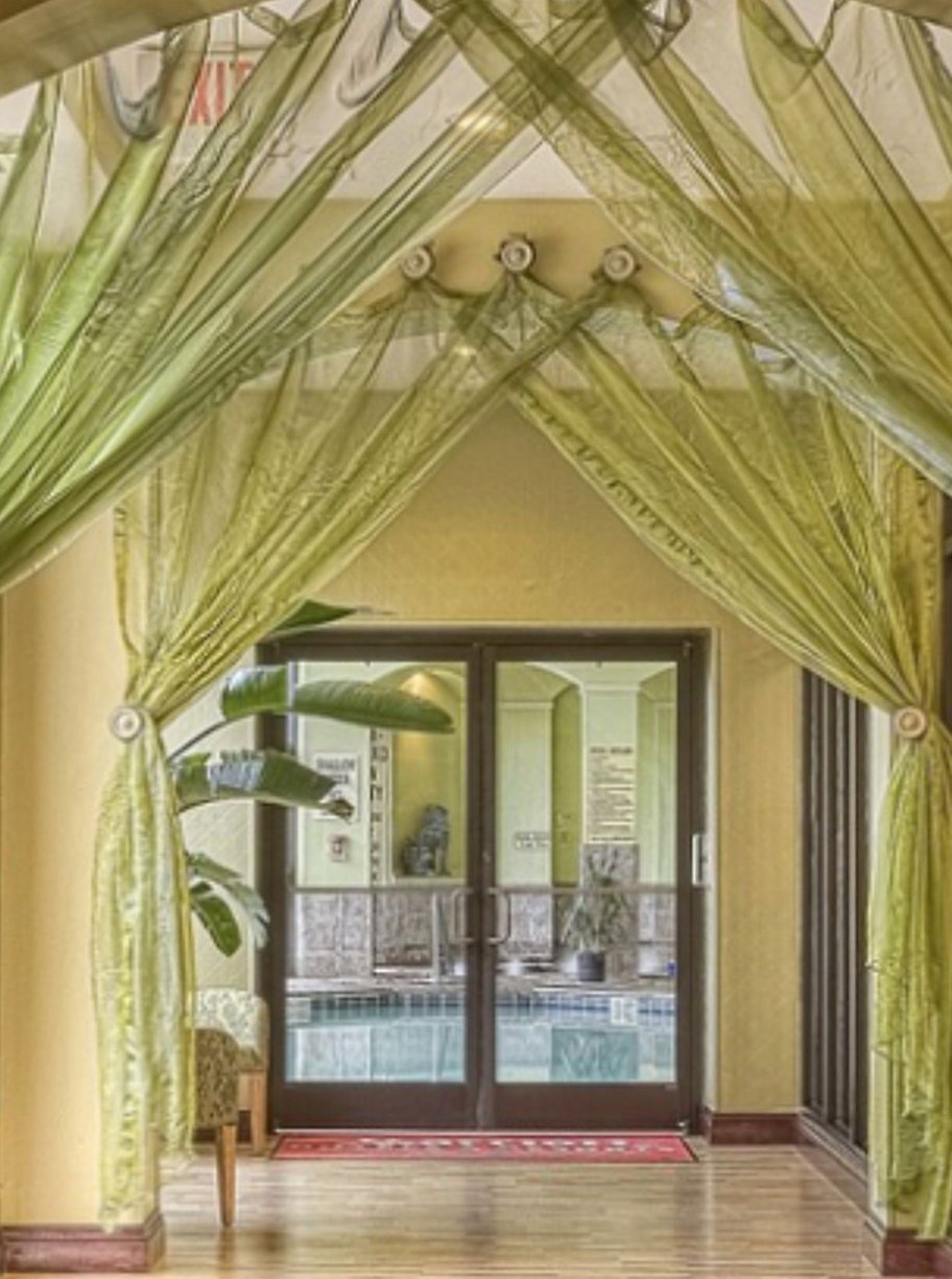 Hotel indoor pool seen through glass doors, framed by draped green curtains
